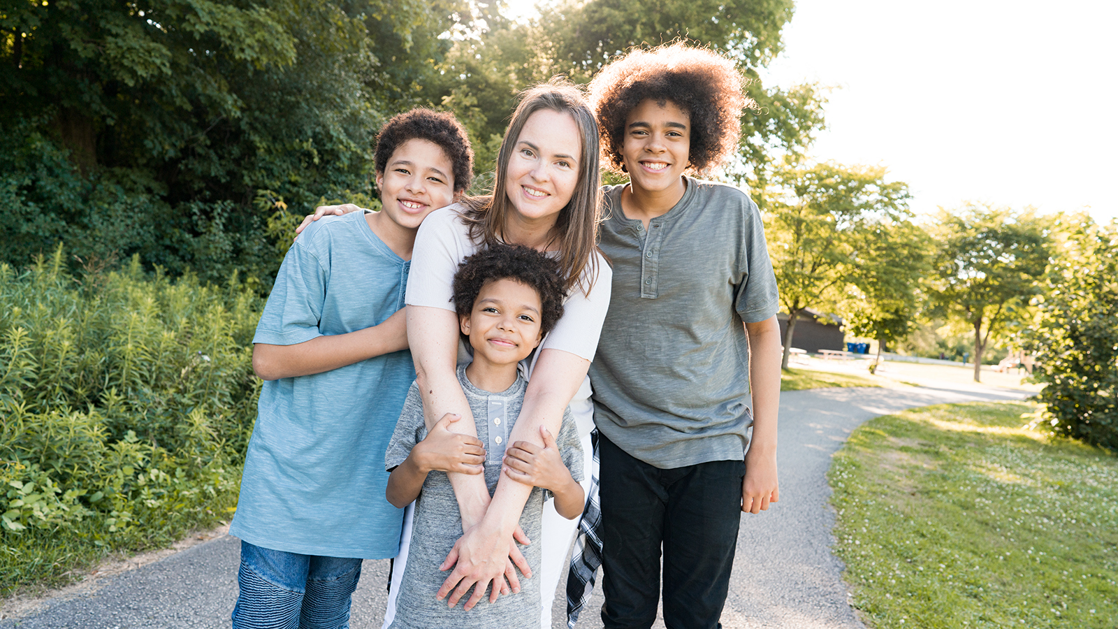 Thanks to KVC's Connect Parent Group, a mom with three sons smiles as they embrace outside in the sunshine because of the skills they developed to improve their relationship. 